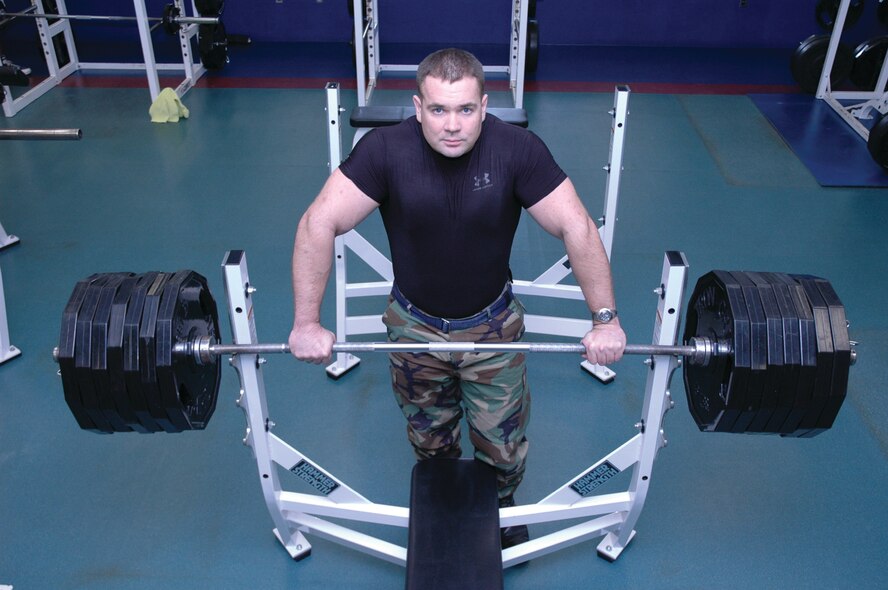 OSAN AIR BASE, Republic of Korea --  Staff Sgt. Michael Schwanke stands behind a bar with 675 pounds, the same amount of weight he lifted at the 8th Army powerlifting competition. In order to get that much weight on a bar, 14 45-pound plates were added. Through years of workout, he has developed a 47 inch chest, 18.5 inch biceps and 29.5 inch thighs. (U.S. Air Force photo by Tech. Sgt. Michael O'Connor)