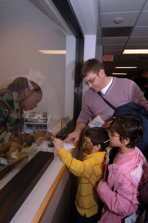 Tony Gunther, son of Chief Master Sgt. John Gunther, 437th Security Forces Squadron superintendent, helps Master Sgt. Gloria Thompson, 437th Comptroller Squadron, stamp his $200 travel voucher at the children’s deployment line while Chief Gunther and his daughter, Gloria, look on. (U.S. Air Force photo/Staff Sgt. April Quintanilla)