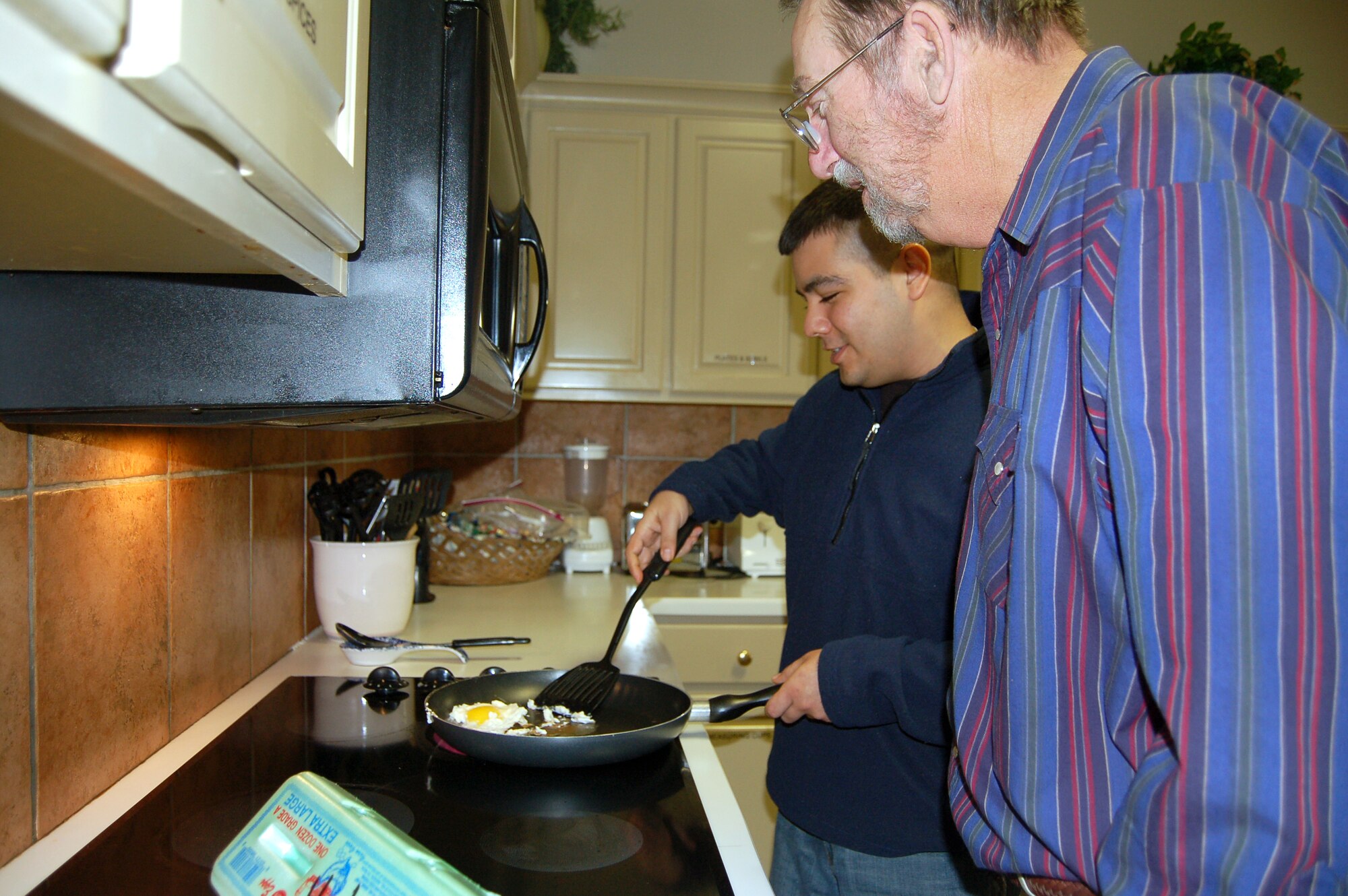 Senior Airman Edward Alvarado and Tom Pennington strike up a conversation as Airman Alvarado cooks an egg in the kitchen of the Fisher House at Lackland Air Force Base, Texas.  Residents at the Fisher House often become quite close because of their shared hardships. The Fisher House offers a place to stay for family members of people hospitalized at military medical centers.  (U.S. Air Force photo/Staff Sgt. Jeremy Larlee)