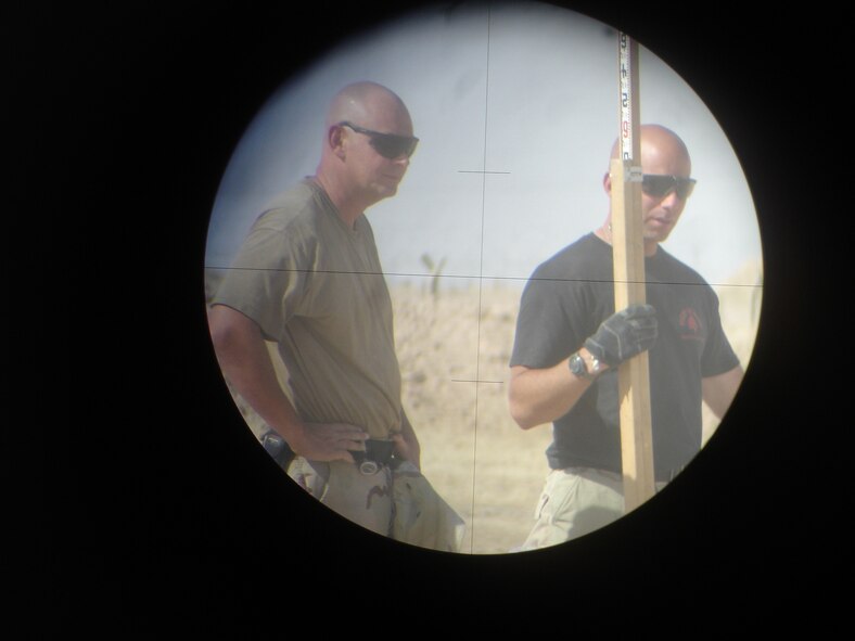 Civil engineers are photographed through a survey scope as they perform their duties at a forward deployed location. Courtesy photo.
