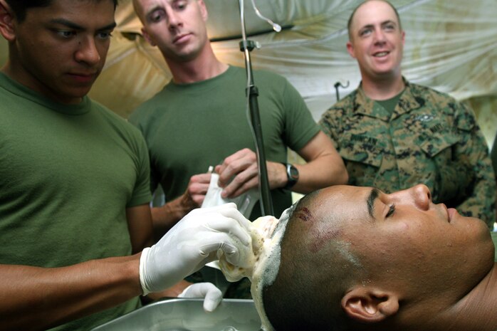 Lance Cpl. Jacob E. House, Marine Wing Support Squadron 171 combat engineer and native of Midland, Mich., lies awake while his wound is cleaned by Petty Officer 3rd Class Alfred R. Vargas. House was injured while pounding a stake to secure the armory here Aug. 21.