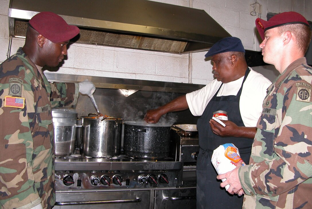 Left to right: Army Sgt. Steven Craig Wright, a 32-year-old 82nd Airborne Division cook from Jefferson, S.C., his assistant, Pfc. Michael Wayne Bennett, 18, from Bristow, Okla., and Algiers restaurant owner George V. Rainey, 74, prepare dinner at St. Mary's Place Mission in Algiers, an old neighborhood in New Orleans, Sept. 18. Photo by Gerry J. Gilmore