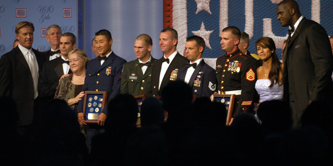 The United Service Organizations' five Servicemembers of the Year are joined by various luminaries while they display their awards on stage during the annual USO gala in Washington on Sept. 14. From left are football star John Elway; Air Force Gen. Richard B. Myers, chairman of the Joint Chiefs of Staff; singer/songwriter Henry Rollins; actress Kath Kinney; Coast Guard Petty Officer 3rd Class Lee O. Zee; Army Spc. William T. Groves; Navy Chief Petty Officer James P. Morgan; Air Force Tech. Sgt. Joseph K. Carter; Marine Staff Sgt. Matthew T. Anderson; TV personality Leeann Tweeden; and basketball star Shaquille O'Neal. Photo by Samantha L. Quigley
