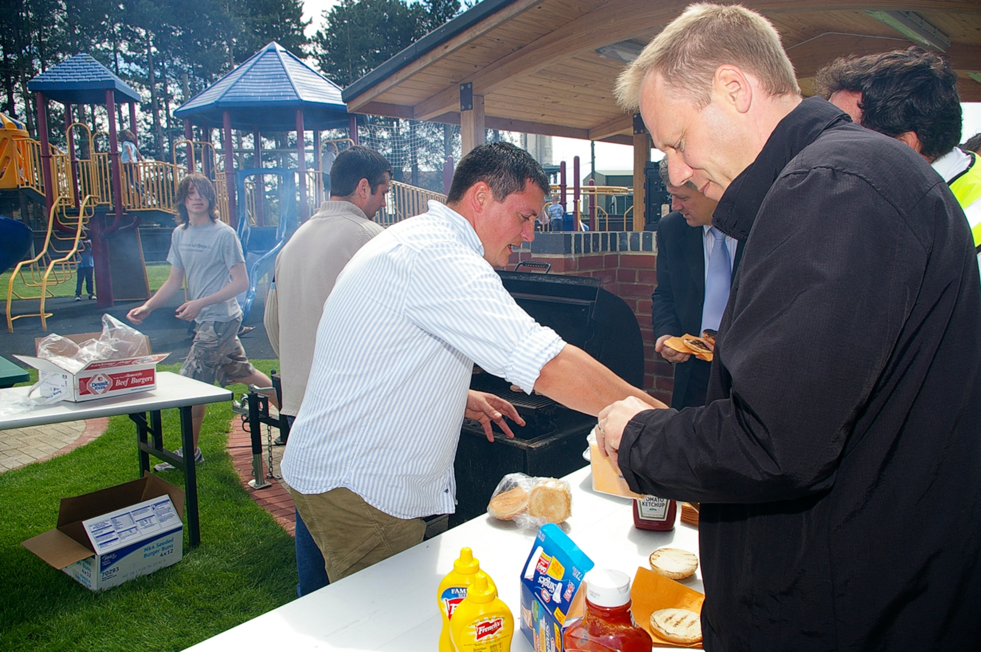 Dave Wainwright, center, 100th Services Squadron Outdoor Recreation director; Joe Twilla, second left, outdoor rec, and Jacob Dybdahl, left, 16, summer hire and volunteer at outdoor rec, barbecue burgers for members of the 100th Civil Engineer Squadron and children from the youth center at the opening of Heritage Park July 3. (U.S. Air Force photo by Karen Abeyasekere)
