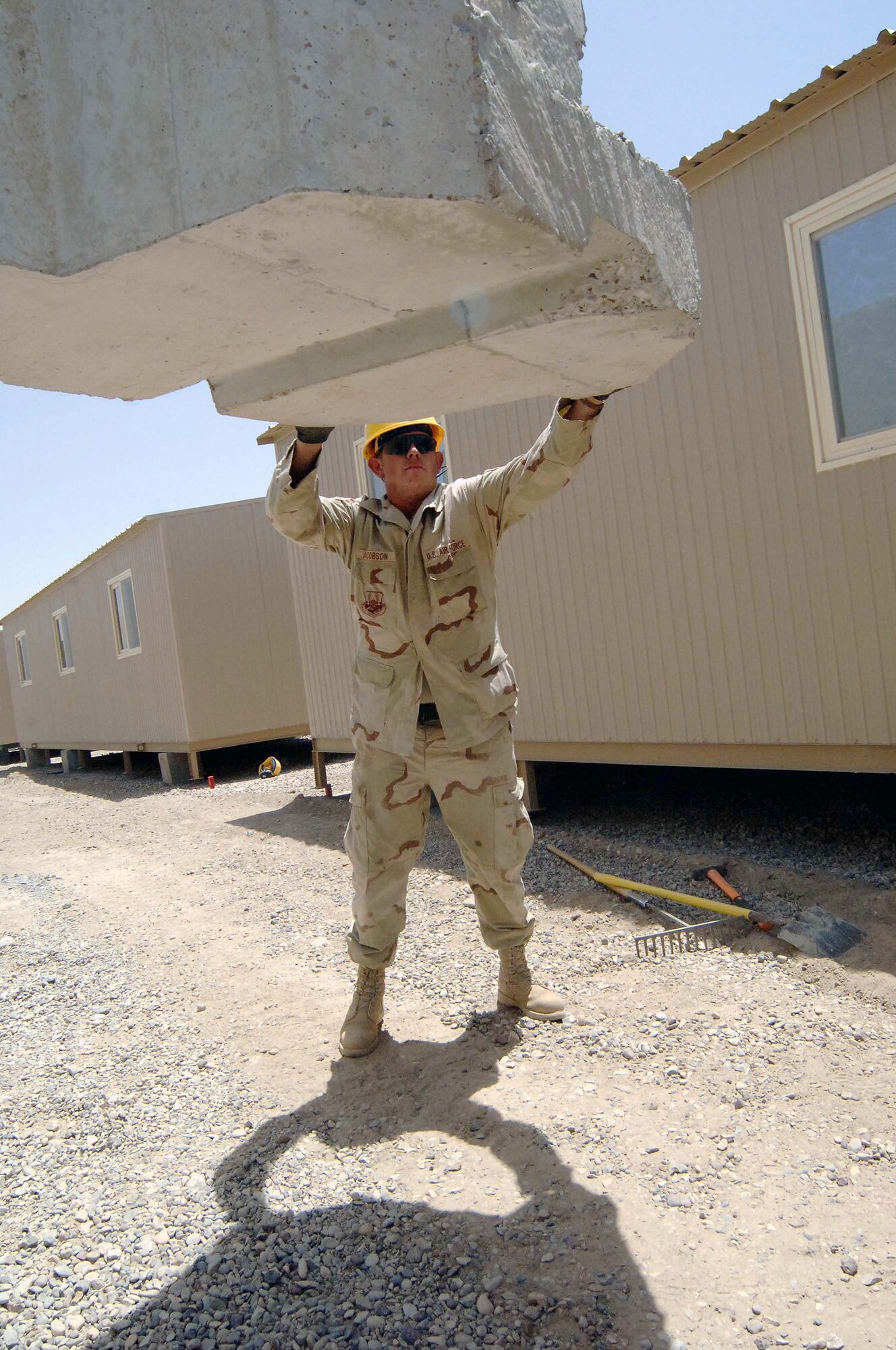 Senior Airman Aaron Jacobson guides a five-ton T barrier into place June 27 at Sather Air Base, Iraq.  The barrier sections, moved by large cranes, are part of a concrete wall being pieced together for protection against incoming rockets and mortars.  Airman Jacobson is a pavement specialist with the 447th Expeditionary Civil Engineer Squadron.  (U.S. Air Force photo/Tech. Sgt. Russell Wicke) 