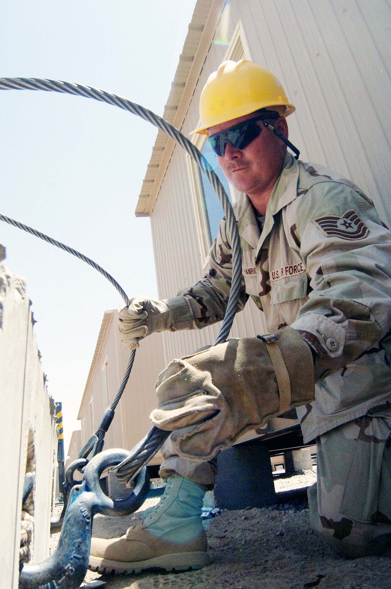 Tech. Sgt. Scott Hamrick hooks up cables from a crane to a concrete T barrier that is ready to be moved into position June 27 at Sather Air Base, Iraq. The barriers are part of a concrete wall being pieced together for protection against incoming rockets and mortars.  Sergeant Hamrick is a pavement specialist with the 447th Expeditionary Civil Engineer Squadron. (U.S. Air Force photo/Tech. Sgt. Russell Wicke) 