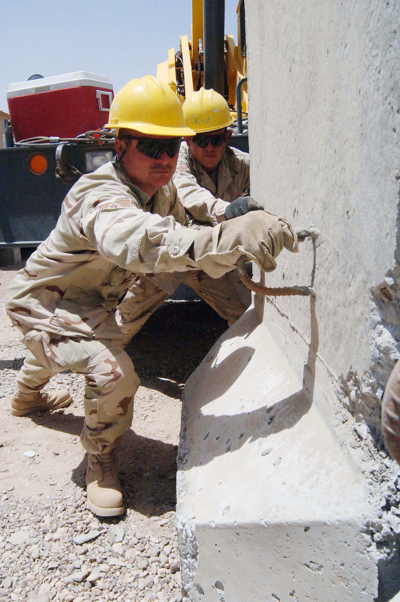 Tech. Sgt. Scott Hamrick (front) and Senior Airman Aaron Jacobson guide a concrete T barrier into place June 27 at Sather Air Base, Iraq.  The barrier sections, moved by large cranes, are part of a concrete wall being pieced together for protection against incoming rockets and mortars.  Sergeant Hamrick and Airman Jacobson are pavement specialists with the 447th Expeditionary Civil Engineer Squadron.  (U.S. Air Force photo/Tech. Sgt. Russell Wicke) 