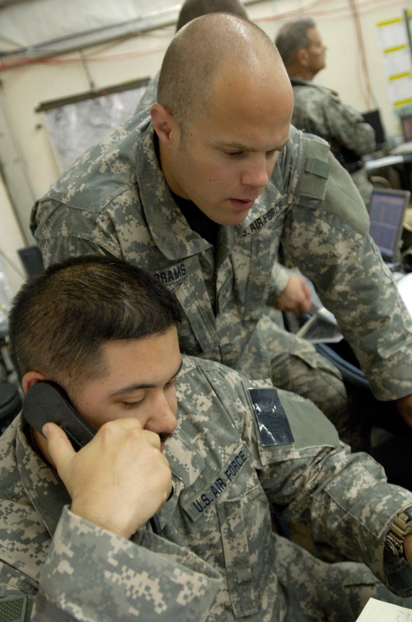 Senior Airman Logan Abrams (right) observes as Tech. Sgt. Mike Cmelik talks to a B-1 Lancer pilot during a bombing mission taking place south of Baghdad on June 25.  Sergeant Cmelik and Airman Abrams are joint terminal attack controllers with the 15th Expeditionary Air Support Operations Squadron and are assigned to provide support to the U.S. Army's 2nd Brigade combat team, 3rd Infantry Division at Forward Operating Base Kalsu, Iraq. (U.S. Air Force photo/Master Sgt. Jim Varhegyi)