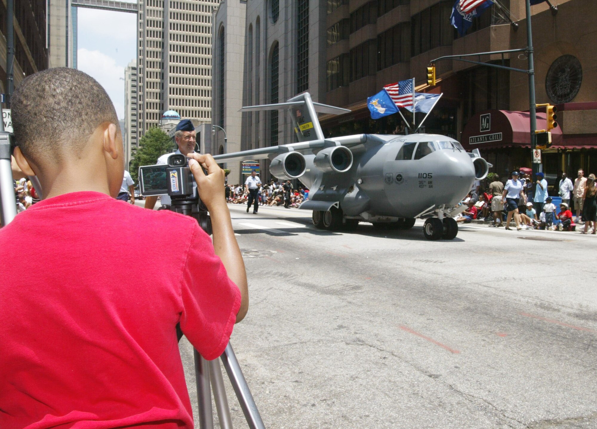 Nacoleon Hillsman, a young cameraman, records the Mini C-17 Globemaster as it makes its way down the parade route while participating in the "Salute 2 America" parade held in downtown Atlanta during 4th of July celebrations. The Mini C-17 Globemaster and its crew are from Charleston Air Force Base, South Carolina.(U.S. Air Force Photo/Don Peek)
