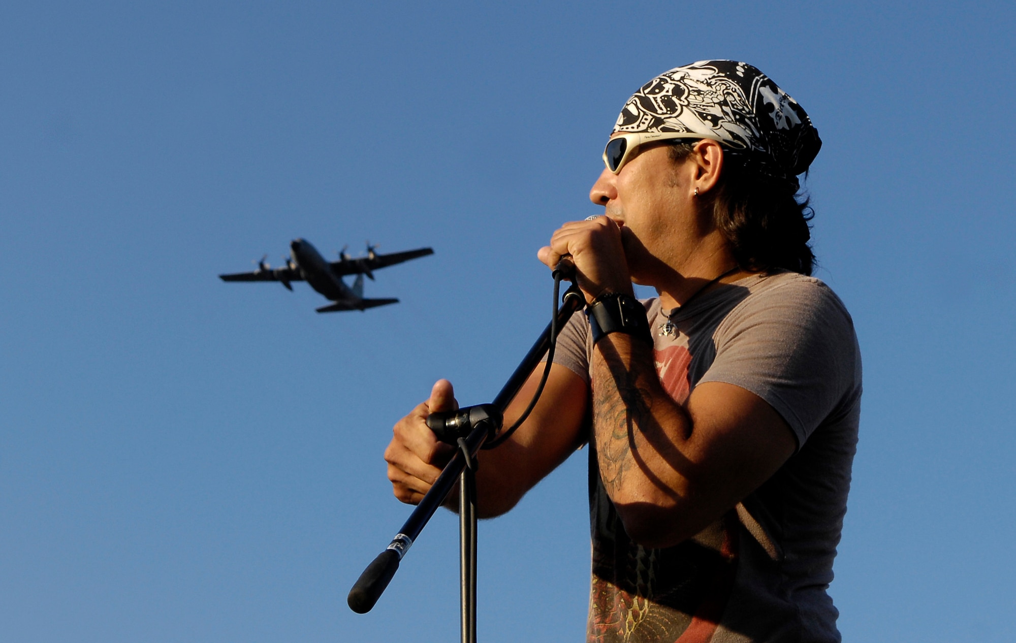 Country music artist Donovan Chapman sings the National Anthem as a C-130 performs a fly-by to start the Donovan Chapman Concert and Tops in Blue Show on archery field at the Saint Louis Science Center, July 6. The concert and show were part of Air Force week here. (U.S. Air Force photo/Staff Sgt. Brian Ferguson) 