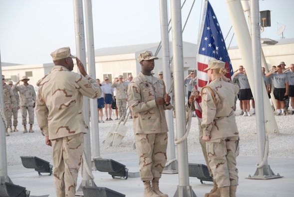 The Desert Eagle Team honor guard lowers the flag during reveille at the flag poles near Memorial Plaza in Coalition Compound. The base participated in several activities throughout the day to include; a triathalon, barbecue, darts, limbo and live entertainment. (U.S. Air Force photo by Airman 1st Class Ashley Tyler)
