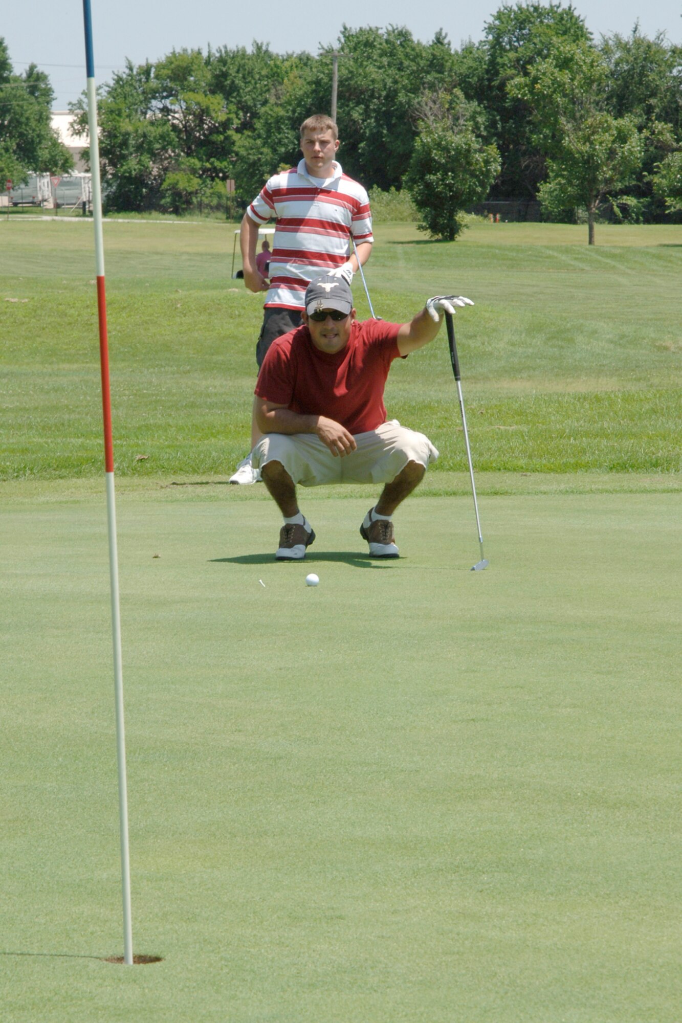 MCCONNELL AIR FORCE BASE, Kan. -- Senior Airman Nicholas Muche, 22nd Contracting Squadron, waits for his turn to put as Staff Sgt. Luis Torres, 22nd Air Maintenance Squadron, lines up a put at the base golf course July 6 during the Rodeo golf tournament. Sergeant Torres and Airman Muche participated in the Rodeo golf tournament to support the McConnell’s Rodeo team who will be competing in this year’s competition July 22-28 at McCord Air Force Base, Wash. (Photo by Airman 1st Class Roy Lynch)