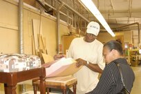 Longtime woodcraftsman Freddie Cloyd shows Camellia Brissett-Fulk, Lackland Arts and Crafts programmer, a couple of wood stools he is refinishing at the Wood Shop at Lackland Air Force Base, Texas. Mr. Cloyd is known for treating the Wood Shop staff to lunch on Tuesdays. (USAF photo by Lilly Flores-Janecek)                                