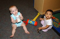 One-year-old Jamie Lynn Eubanks takes a drink from her bottle while Zahira Momna, 11 months, plays with a set of keys during Children's Playgroup at Lackland Air Force Base, Texas. This is Jamie's first time at Playgroup, while Zahira had been coming since Playgroup was at its previous location in the Child Development Center. Jamie is the daughter of Wendy and Army 1st Lt. Jeremy Eubanks, of the 108th Aviation Regiment. Zahira is the daughter of Nazneen and Senior Airman Momna Sameer of the Air Force Intelligence Analysis Agency. (USAF photo by Mondo Flores)                              