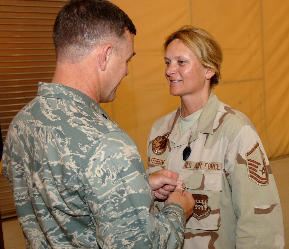 SATHER AIR BASE, Iraq – Master Sgt. Luann Van Peursem (right), 447th Expeditionary Logistics Readiness Squadron,  receives the Air Force Commendation Medal with Valor from Brig. Gen. Burton Field, 332nd Air Expeditionary Wing commander, July 12 for providing first aid to Airmen injured by a rocket attack here in June. Sergeant Van Peursem led the initial medical response for two Airmen critically injured by shrapnel from an exploding rocket. After the rocket hit outside her building she quickly responded to moaning and cries for help. As she was providing aid to the first Airman, she heard additional cries in the distance. She passed care of the first victim to others and ran to the other victim. By herself she moved him to a bunker for protection and rendered proper aid. She then managed the care for both victims until medical personnel arrived. The Valor device is not for peacetime acts of service. The Valor decoration was awarded to Sergeant Van Peursem to recognize the selfless action of placing herself in harm’s way during an attack to provide aid to multiple injured Airmen. (U.S. Air Force photo/Tech. Sgt. Russell Wicke) 