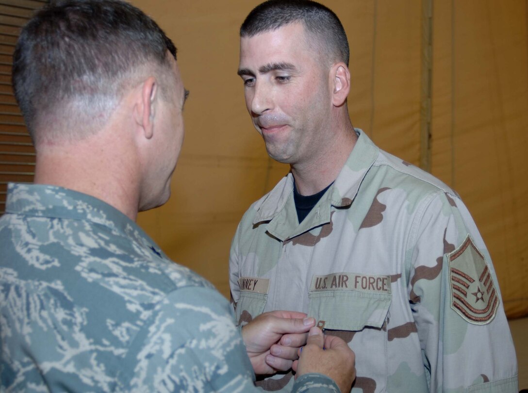SATHER AIR BASE, Iraq – Master Sgt. Joseph Kinney (right), 447th Expeditionary Logistics Readiness Squadron,  receives the Air Force Commendation Medal with Valor from Brig. Gen. Burton Field, 332nd Air Expeditionary Wing commander, July 12 for providing first aid to another Airman injured by a rocket attack here in June. Sergeant Kinney led the initial medical response to the Airman after dialing 911. He found the Airman had critical shrapnel injuries to the face, eye and thigh. In addition the victim suffered difficulty breathing. After repositioning the Airman to open his airway, Sergeant Kinney cleaned and treated the wounds until medical personnel arrived. The Valor device is not for peacetime acts of service. The Valor decoration was awarded to Sergeant Kinney to recognize the selfless action of placing himself in harm’s way during an attack to provide aid to the injured Airman. (U.S. Air Force photo/Tech. Sgt. Russell Wicke) 