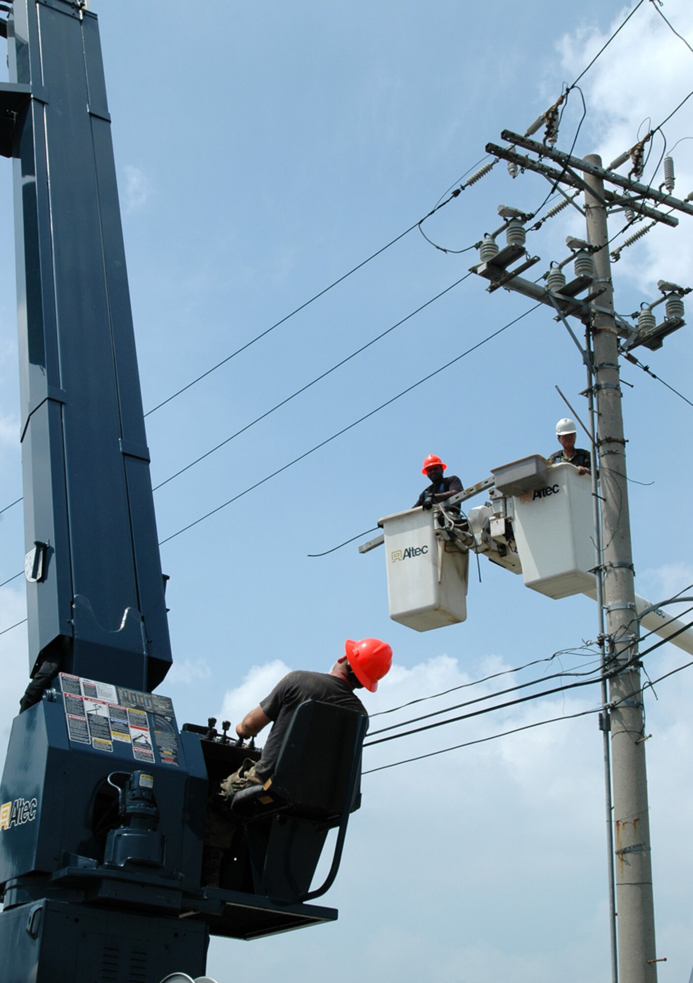 OSAN AIR BASE, Republic of Korea -- Members of the 51st Civil Engineer Squadron Electric Shop work in the heat July 12 to keep Osan up and running.  It is the tremendous efforts of the behind-the-scenes Mongrels that keep quality of life systems like heat and air conditioning running daily. The electric shop plans operations like these extensively to maximize safety and minimize downtime.  Mongrel. Chong "Father" Hwon Yi and Senior Airman Jarvis Jones watch as the oil switch they disconnected gets lowered to the ground with a line truck. One of the last functions of the operation is removing the safety equipment.  Senior Airman Earnest Perkins and Staff Sgt. Dayrone Henry remove a ground set which is clamped into place with insulated sticks rated higher than the 13,800 volts that normally flow through these lines.  (U.S. Air Force photo by Master Sgt. Steven J Goetsch)
