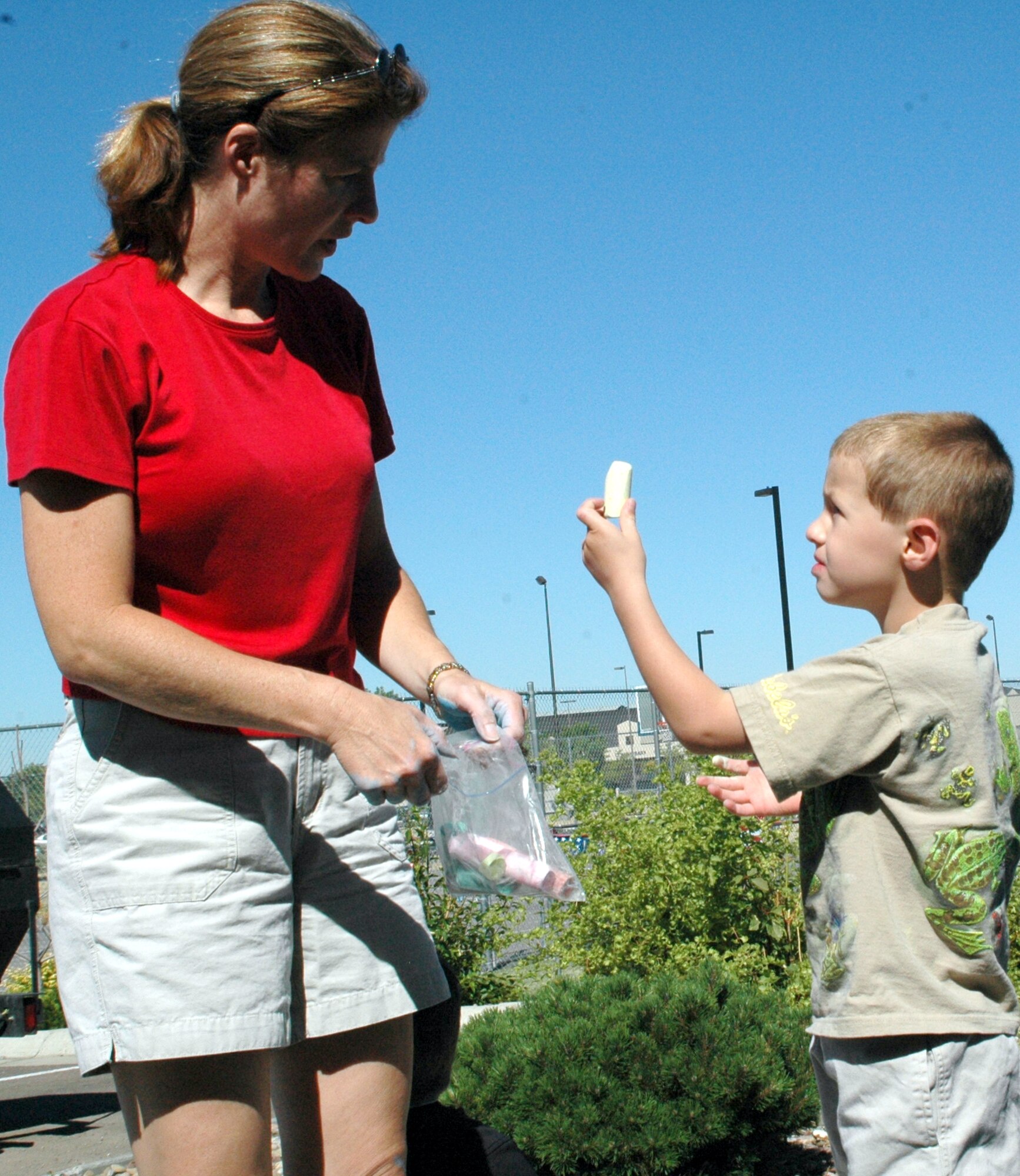 Little Warrior Benjamin, 5, asks mom, Tracy, if he can use the yellow chalk next. More than 100 children participated in the annual Chalk It Up! art contest decorating the sidewalk squares around the Youth Program Center Wednesday. Afterwards, they were treated to a barbecue. (U.S. Air Force photo / Valerie Mullett)