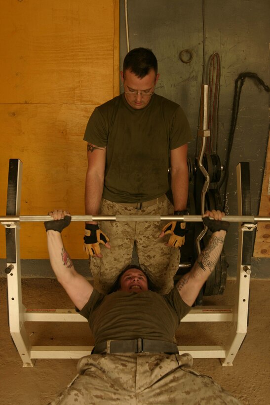 HADITHA, Iraq ? Staff Sgt. John Wear, staff noncommissioned-officer-in-charge of the Intelligence section, Headquarters and Service Company, Task Force 1st Battalion, 3rd Marine Regiment, Regimental Combat Team 2, assists a fellow Marine with his bench press in the gym located in the Hadithah forward operating base.