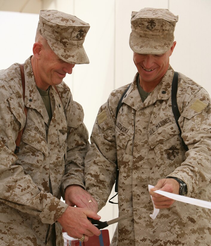 AL ASAD, Iraq- Lt. Col. Stephen Liszewski, commanding officer of Task Force Military Police, 1st Battalion, 12th Marine Regiment, holds the ribbon during the ceremony as Brig. Gen. Timothy C. Hanifen, commanding officer of 2nd Marine Aircraft Wing (Forward), cuts the ribbon to signify the opening of the new military working dog kennels, July 18.  The new facility was built to accommodate the dogs and features a bathing sink, an improved obedience course and break yard, and includes increased kennel capacity.