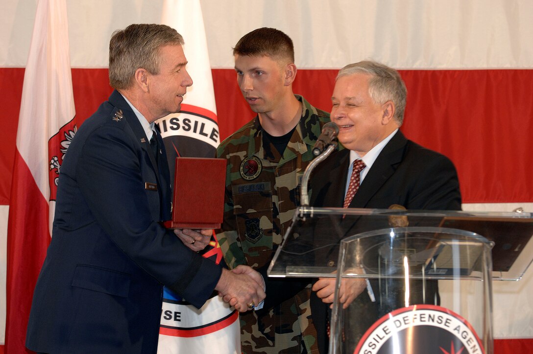 VANDENBERG AIR FORCE BASE, Calif. -- Missile Defense Agency Director Lt. Gen. Trey Obering presents a pin from an interceptor missile to Polish President Lech Kaczynski during a press conference on July 17 in the 76th Helicopter Squadron hangar.  Standing between them is Staff Sgt. Radoslaw Ciesielski, a native Polish speaker and the NCOIC of facility maintenance and operations for the 30th Space Wing and 14th Air Force headquarters building.  The Polish president came to Vandenberg to tour missile defense facilities located on the base and meet with Missile Defense Agency officials.  (U.S. Air Force photo/Tech. Sgt. William Greer)
