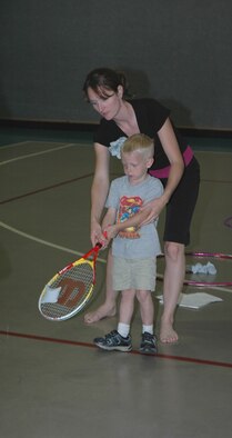 Kelley Suggs, health education program manager at the HAWC shows Lucas, 5, how to properly hold a tennis racket during a tennis clinic at the YPC. The clinic was part of a week-long effort to promote fitness in kids.  (U.S. Air Force photo / Airman 1st Class Dillon White)