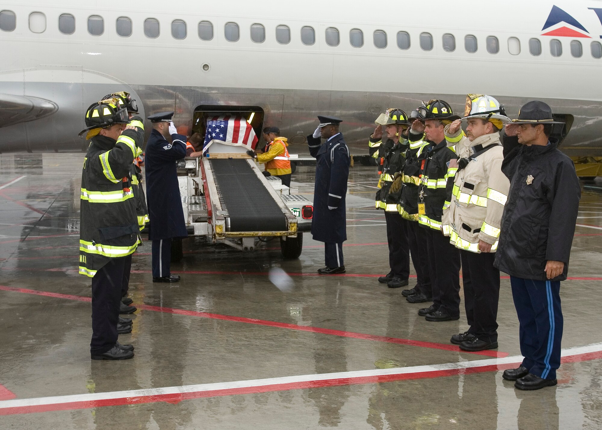 HANSCOM AFB, Mass. -- From left, nearest to airplane ramp, Patriot Honor Guard Staff Sgts. Philip Pelletier and Lucien Blake render salutes as the remains of Staff Sgt. Donald Michaud are lowered from a Delta Airlines jet at Logan Airport. Joining the sergeants are members of the Logan Airport Fire Department and a member of the Massachusetts State Police. (U.S. Air Force photo by David Turner)