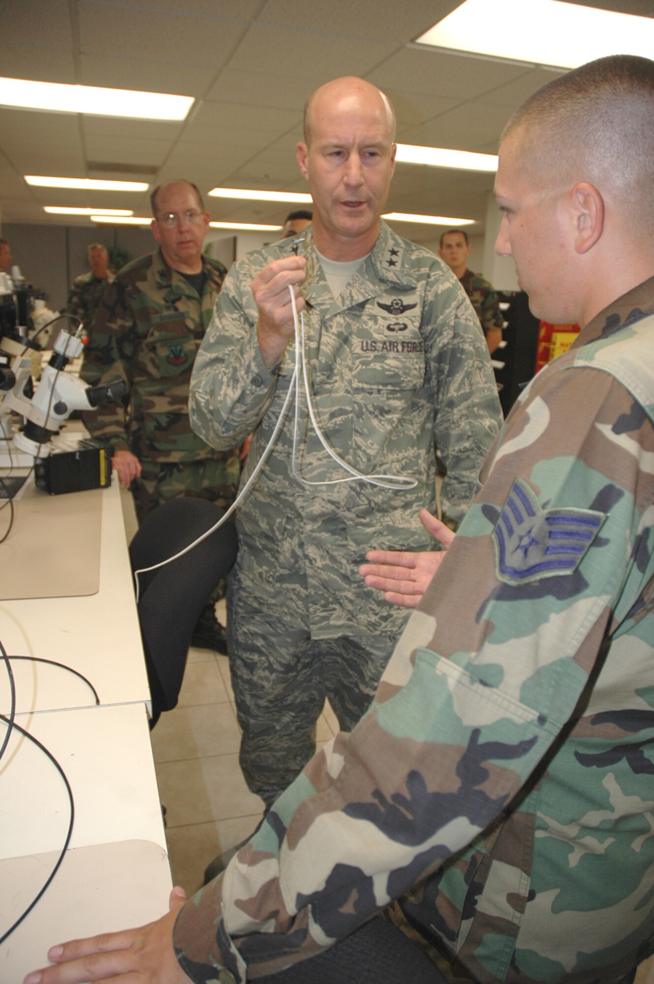 Maj. Gen. Douglas L. Raaberg, the director of air and space operations at Headquarters Air Combat Command, Langley Air Force Base, Va., holds up a power cord for the Blue Force airborne tracking system and talks with Staff Sgt. Robert Brutto, an AFREP technician here, about how it was repaired. General Raaberg stopped by the AFREP shop during his visit to D-M this week. (U.S. Air Force photo/Staff Sgt. Jake Richmond)