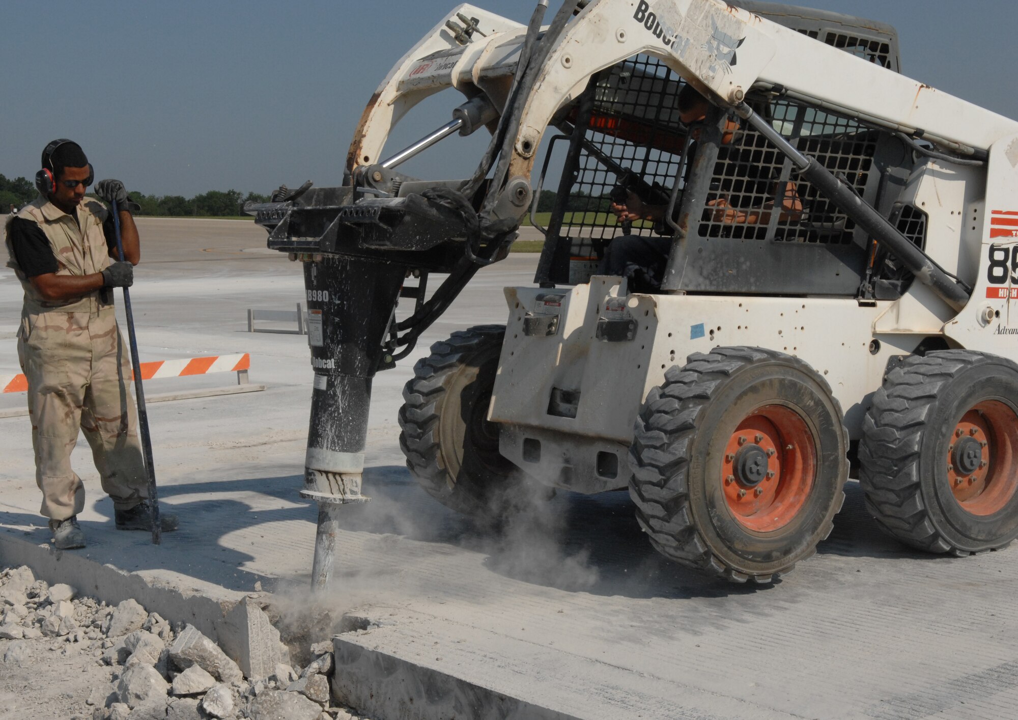 WHITEMAN AIR FORCE BASE, Mo. -- Staff Sgt. Derek Phillips, 823rd RED HORSE Squadron, stands by as Senior Airman Zachary Norris, 823rd RHS, uses a Bobcat to demolish a concrete slab. (U.S. Air Force photo/Staff Sgt. Jason Barebo)