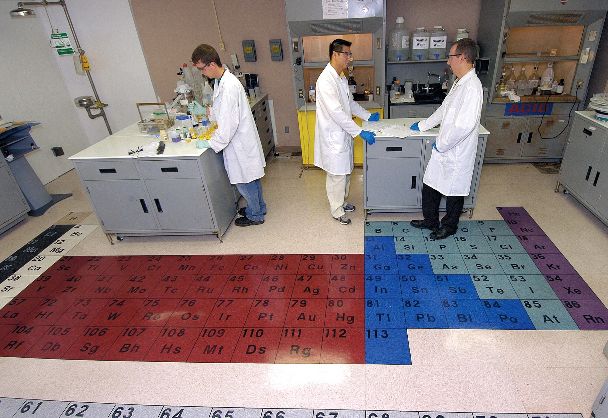 A colorful periodic table now graces the floor of the 76th Maintenance Wing Electroplating Lab, an idea of chemist Chris Mance, right, who did the work with help from chemist David Nguyen, center. Fellow chemist Carson Cameron, left, works in the open design that also now allows easier access to an emergency eye wash station. (Air Force photo by Margo Wright)