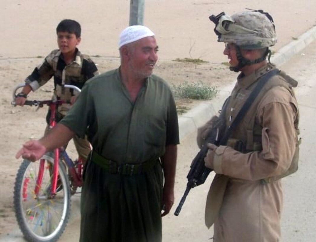 Cpl. James R. Schneider III, a motor vehicle operator and driver for the II Marine Expeditionary Force Headquarters Group commanding officer, speaks with an Iraqi citizen just outside a military housing complex in Baghdadi, Iraq, July 2007.  Schneider deployed to Iraq for seven months in support of Operation Iraqi Freedom.