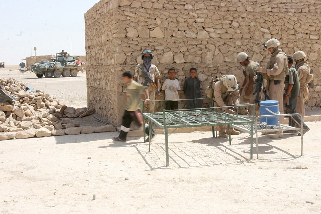 COMBAT OUTPOST RAWAH, IRAQ, (JULY 24, 2007) – Several Marines from Company C, 1st Light Armored Reconnaissance Battalion, Regimental Combat Team 2, stand guard as a Navy corpsman prepares to treat an Iraqi civilian with a foot injury during ‘Operation Mawtini.’ The battalion is part of the regimental-wide operation which kicked off July 15, 2007. Official Marine Corps Photo By Cpl. Ryan C. Heiser.
