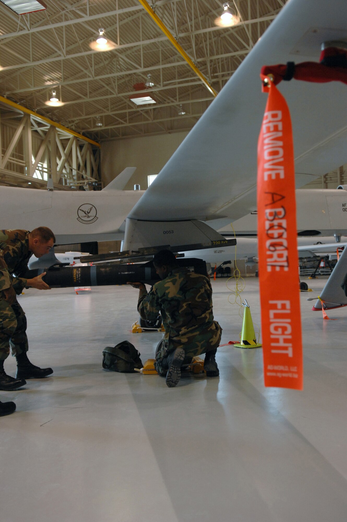 Air Force Tech. Sgt. Brendan Schlaack (left) and Staff Sgt. Phillip Carter, both 57th Maintenance Group F-22A lead standardization crew members, attach a replica of a AGM-114 Hellfire missile onto an MQ-1 Predator during training July 18, 2007, at Creech Air Force Base, Nev. F-22A weapons loaders from Nellis come to Creech every other month for proficiency training on loading missiles onto the Predator and performing actions required to safety the airplane. Such training is necessary in case a Predator will be forced to land at Nellis AFB due to bad weather or runway problems at Creech AFB. (U.S. Air Force Photo by Senior Airman Larry E. Reid Jr.)
