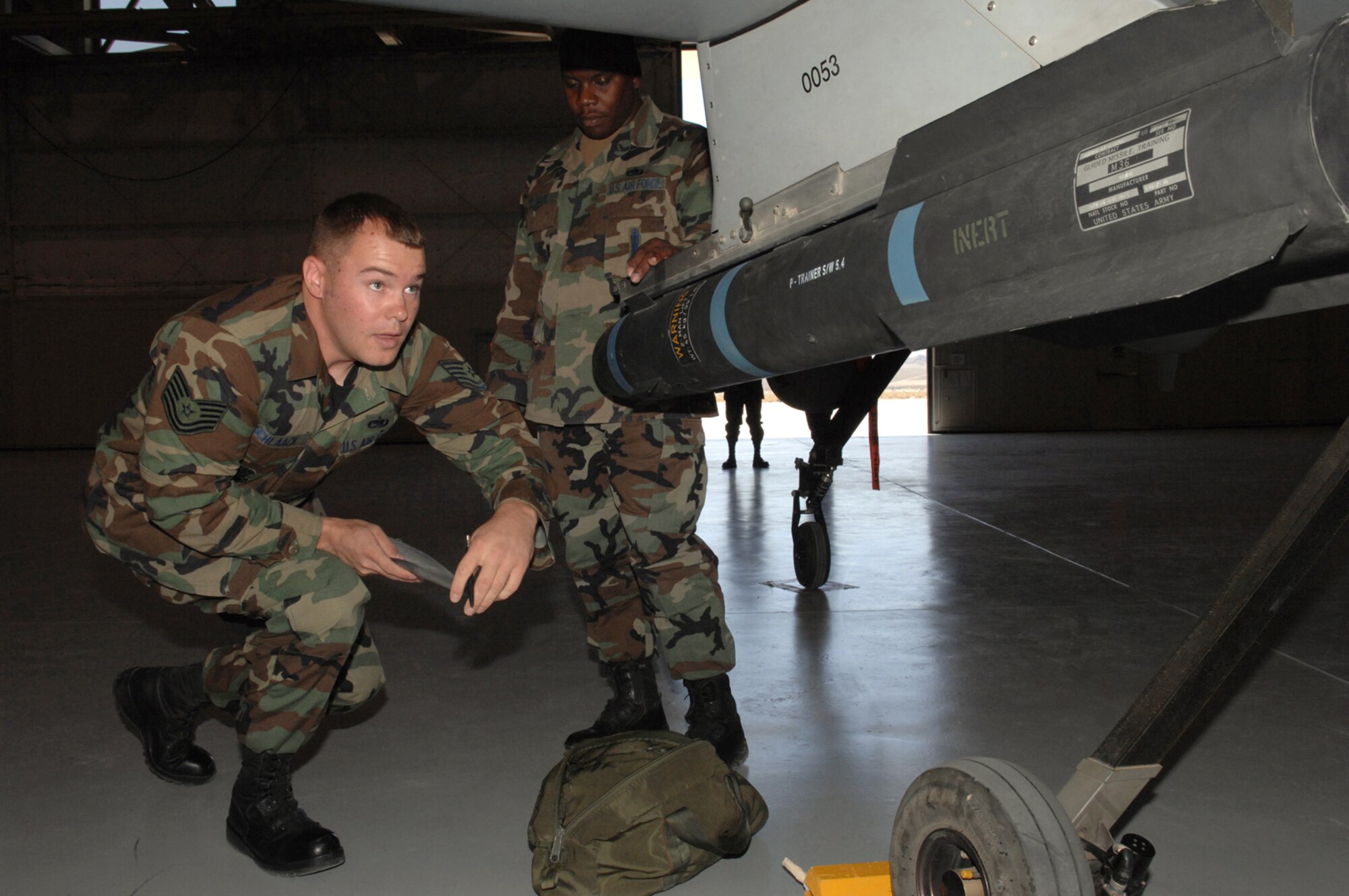 Air Force Tech. Sgt. Derrick Davis (background), 432nd Aircraft Maintenance Squadron weapons standardization section, observes Tech. Sgt. Brendan Schlaack, a 57th Maintenance Group F-22A lead standardization crew member, during his evaluation, July 18, 2007, at Creech Air Force Base, Nev. F-22A weapons loaders from Nellis come to Creech every other month for proficiency training on loading missiles on the Predator. While Air Combat Command standards require the task to be accomplished within 20 minutes, Airmen at Nellis and Creech raised their own bar and do not settle for anything more than six minutes with no shortcuts, said Sergeant Davis. (U.S. Air Force Photo by Senior Airman Larry E. Reid Jr.)
