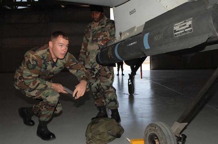 Air Force Tech. Sgt. Derrick Davis (background), 432nd Aircraft Maintenance Squadron weapons standardization section, observes Tech. Sgt. Brendan Schlaack, a 57th Maintenance Group F-22A lead standardization crew member, during his evaluation, July 18, 2007, at Creech Air Force Base, Nev. F-22A weapons loaders from Nellis come to Creech every other month for proficiency training on loading missiles on the Predator. While Air Combat Command standards require the task to be accomplished within 20 minutes, Airmen at Nellis and Creech raised their own bar and do not settle for anything more than six minutes with no shortcuts, said Sergeant Davis. (U.S. Air Force Photo by Senior Airman Larry E. Reid Jr.)

