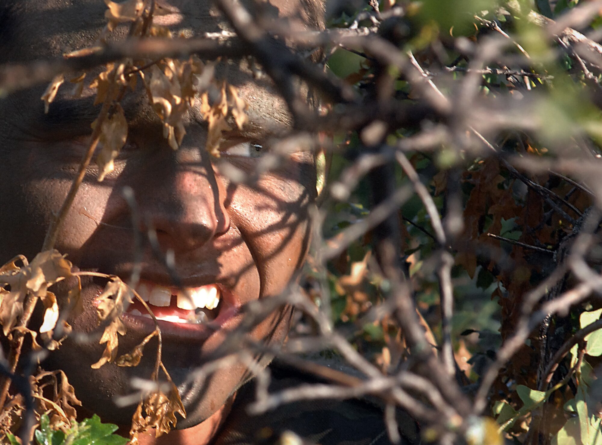Senior Airman Arthur Sgruggs, an "enemy insurgent," stays hidden while scanning for cadets July 13 during Global Engagement, a summer course at the U.S. Air Force Academy in Colorado Springs, Colo.  Global Engagement teaches cadets the expeditionary Air Force concept of deploying, establishing a bare-base operation, executing their mission, defending their base and re-deploying home.  Airman Sgruggs is a security forces instructor from Schriever Air Force Base, Colo.  (U.S. Air Force photo/Tech. Sgt. Larry A. Simmons) 