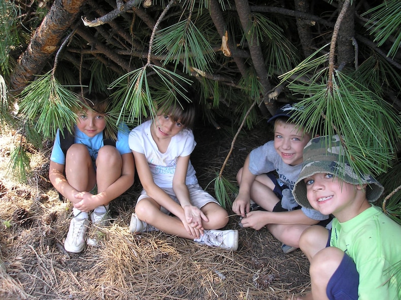 SPOKANE, Wash. – From left, Makyla Carney, Katherine Schmoldt, Issac Detiege and Matthew Lacey sit in a shelter built by instructors from the Survival, Evasion, Resistance and Escape School at Fairchild Air Force Base, Wash. The children attended the Blue Green Summer Youth Camp here July 16 - 20, where they learned a bit about deployed environments and learned coping strategies for separation stresses. The camp is a joint-service camp designed specifically for children with deployed parents. This year, all Department of Defense services were represented through the young campers. (U.S. Air Force photo/ Melissa Still) 