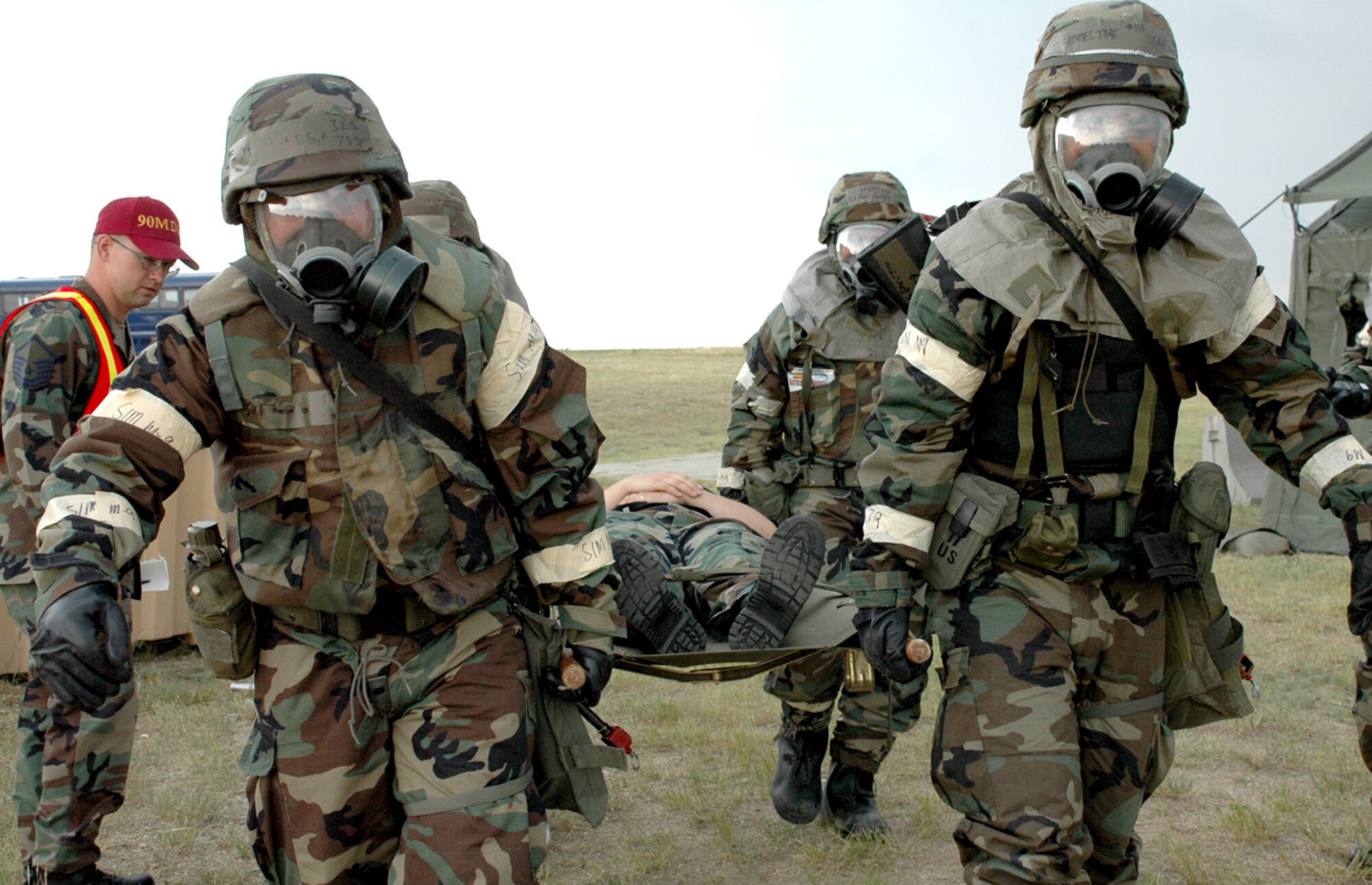 Medics in chemical resistant gear carry a simulated injured volunteer on a stretcher to safety after a simulated mortar attack.