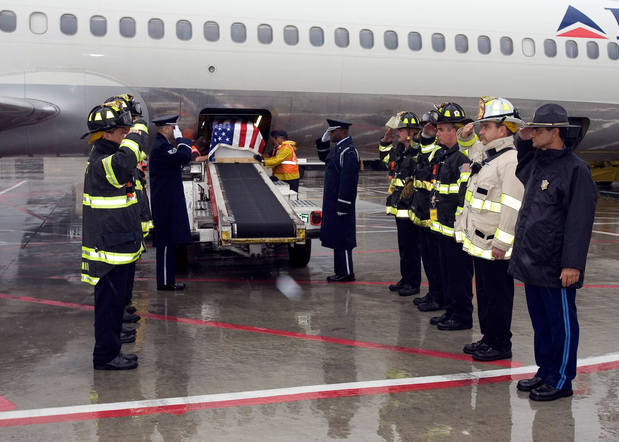 Patriot Honor Guard Staff Sergeants Philip Pelletier (left and nearest to the airplane ramp) and Lucien Blake render salutes as the remains of Staff Sgt. Donald Michaud are lowered from a Delta Airlines jet July 18 at Logan International Airport in Boston. Sergeant Michaud along with two other individuals went scuba diving on Sept. 9, 1978, in Vouliagmeni Lake near Vouliagmenis Point, Greece, and failed to return. An unsuccessful search effort was launched and two weeks later, a presumptive finding of death was declared. In the fall of 2006, a local Greek diving association located wetsuits, diving equipment and human remains believed to be those of the missing individuals. The Armed Forces DNA Identification Laboratory, confirmed the identification of the three missing Americans. Joining the sergeants are members of the Logan Airport Fire Department and a member of the Massachusetts State Police. (U.S. Air Force photo/David Turner)