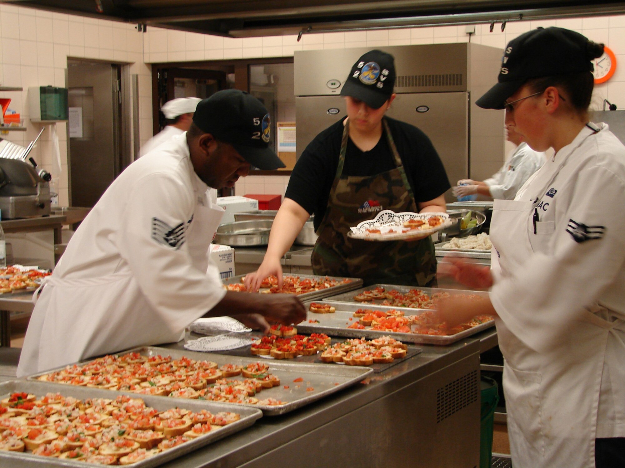 SPANGDAHLEM AIR BASE, Germany -- (Left to right) Staff Sgt.  Jermaine Ireland, Airman 1st Class Brianna Flores, and Airman 1st Class Sherry Mack prepare food for the Colonel Promotion Dinner July 20. The U.S. Air Forces in Europe command chef, Jean Marc Laurent also helped the 52nd Services Squadron Airmen and club staff with food preparation for the event. (U.S. Air Force photo/Heather Klabunde)