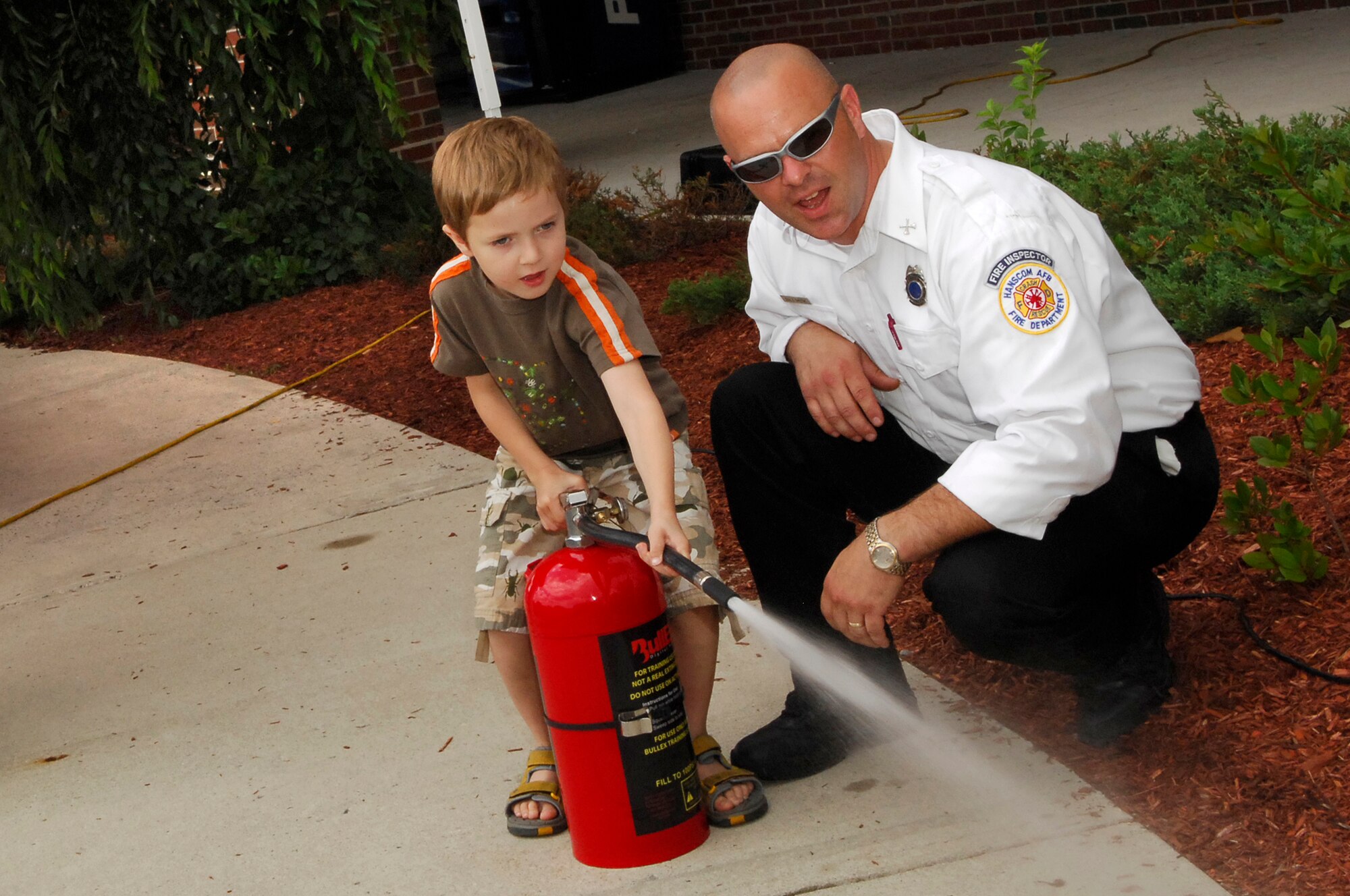 HANSCOM AFB, Mass. -- Firefighter Dale Smith, Fire Prevention chief, assists Chris Rasmussen as he sprays a fire extinguisher during Safety Day. Other agencies that provided safety information to the base populace on Safety Day included the Drug Reduction Program Office, Family Advocacy, 66th Security Forces Squadron and the Health and Wellness Center.  (U.S. Air Force photo by Mark Wyatt)