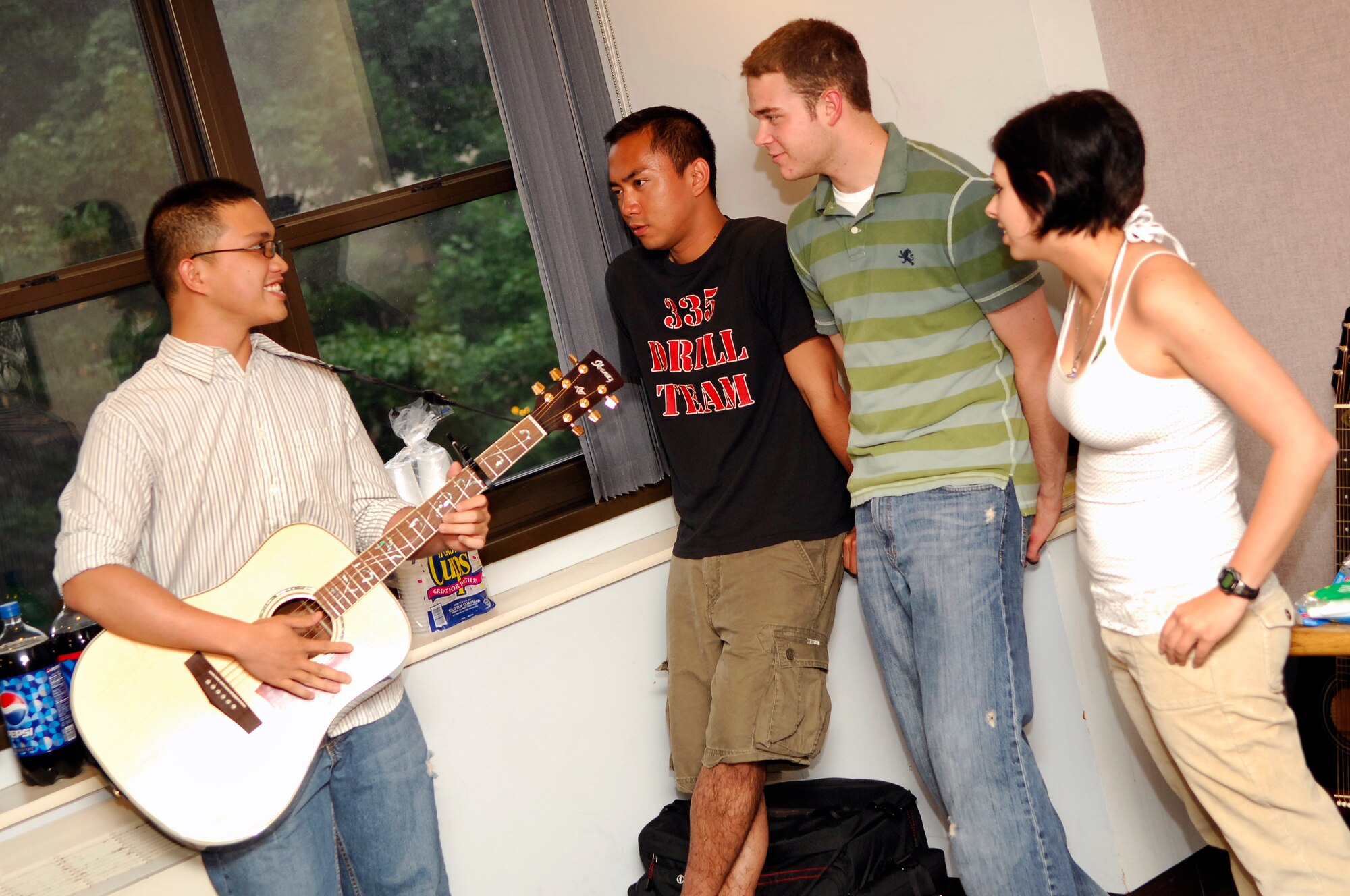 HANSCOM AFB, Mass., -- From left, Airman 1st Class Harold Pastoral, 66th Medical Support Squadron, plays his guitar for fellow dorm residents, Senior Airman James Aguilar, 66th Comptroller Squadron, Airman 1st Class Robert Wiese, 66th Medical Operations Squadron, and Airman Basic Ashley Brock,  66th Air Base Wing Command Post, during a dorm dinner held in building 1510 July 19. The dinner was hosted by Base Chapel personnel. (U.S. Air Force photo by Mark Wyatt)