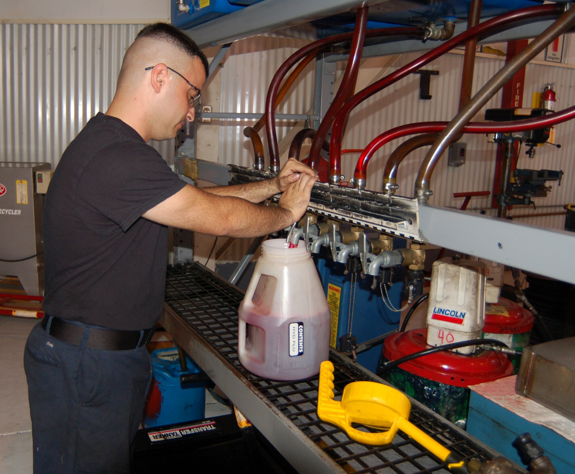 Senior Airman Youndri Reinosa, 436th Logistics Readiness Squadron special vehicle maintainer, utilizes a fluid-distribution system to fill a container of hydraulic fluid. Airman Reinosa helps with the cleanliness and upkeep of his unit's hazardous waste accumulation point. (U.S. Air Force photo/Tech. Sgt. Kevin Wallace)