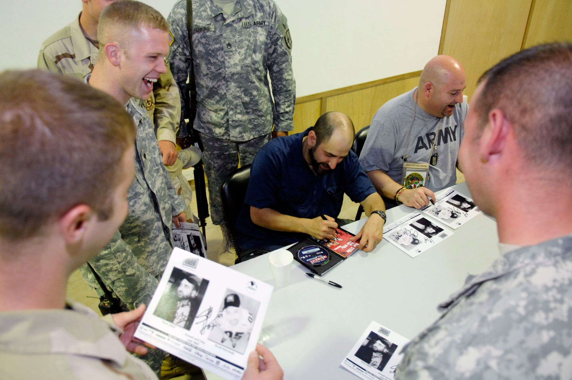 Comedians Dave Attell (center) and Scott Kennedy sign autographs after a USO show for more than 700 Soldiers and Airmen July 25 at Camp Adder, Iraq. This was the second of eight stops in theater for the tour. Mr. Attel is star of Comedy Central's "Insomniac with Dave Attell." (U.S. Air Force photo/Master Sgt. Robert W. Valenca) 
