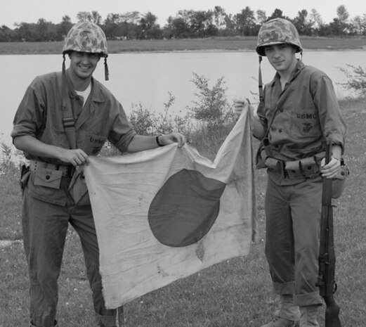 Seaman Andrew Garrison (left), a corpsman with Task Force 2nd Battalion, 2nd Marines, Regimental Combat Team 5, holds a Japanese flag captured during a simulated World War II battle, in Auburn Ind., August, 2007. Garrison has participated in over 30 reenactments and plans to do more once he returns from his deployment in western al-Anbar province, Iraq.  Garrison hopes to one day own a tank and a 1940s Jeep.