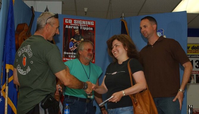 Laura James shakes counrty music singer Aaron Tippin's hand before getting his autograph and a photo taken with him at the autograph session sponsored by the Malmstrom base exchange. Tech. Sgt. Ken James, 341st Missile Security Forces Squadron and Mr. Tippin's piano player, Mike Maiocco, are also pictured. Mr. Tippin was in town to perform at the Montana State Fair. His wife, Thea, is originally from Great Falls. (U.S. Air Force photo/Valerie Mullett)                      