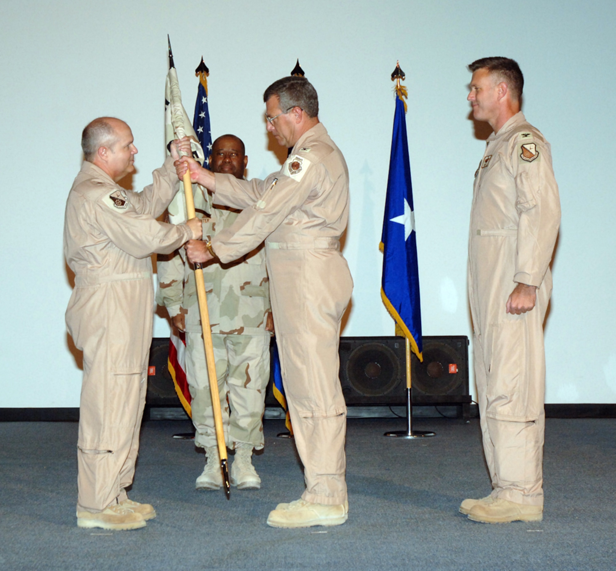 Brig. Gen Charlie Lyon, 379th Air Expeditionary Wing commander (left), passes the 379th Expeditionary Operations Group guidon to incoming commander Col. Robert Gass (center) during a change-of-command ceremony Thursday. Colonel Gass assumed command of the 379th EOG from outgoing commander Col. William Mullins (right). (U.S. Air Force photo by Airman 1st Class Ashley Tyler)