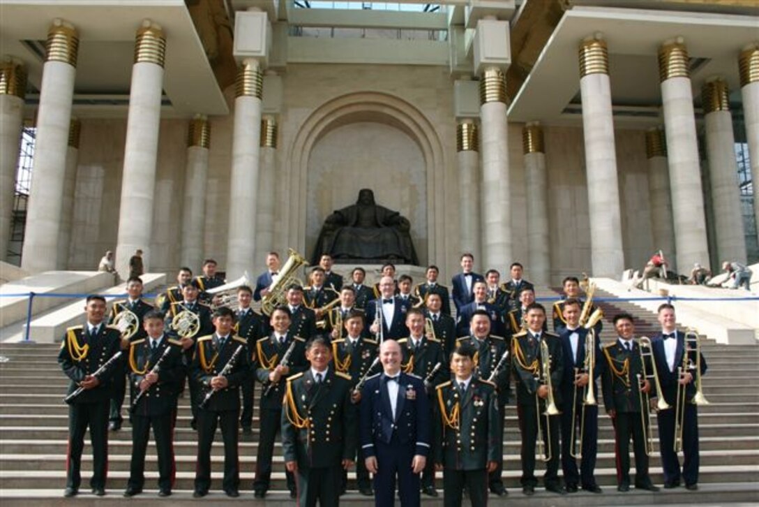 Major Matt Henry and Pacific Brass pose with members of the Mongolian Armed Forces Band outside near majestic Mongolian architecture.