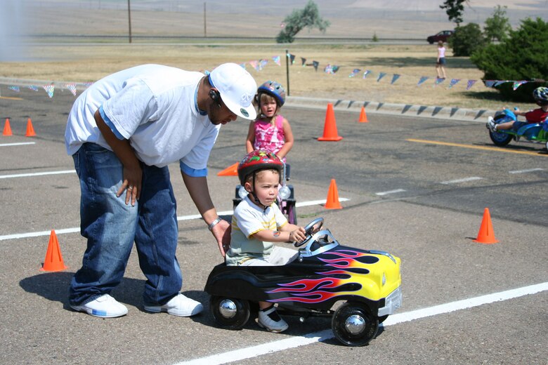 Senior Airman Frank Turner, 341st Maintenance Operations Squadron, pushes Little Warrior, Trévon, 3, through a driving obstacle course at the "Cruisin' the Summer" base picnic July 27.  (U.S. Air Force photo/Senior Airman Eydie Sakura).
