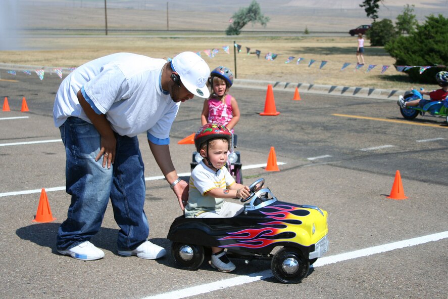 Senior Airman Frank Turner, 341st Maintenance Operations Squadron, pushes Little Warrior, Trévon, 3, through a driving obstacle course at the "Cruisin' the Summer" base picnic July 27.  (U.S. Air Force photo/Senior Airman Eydie Sakura).
